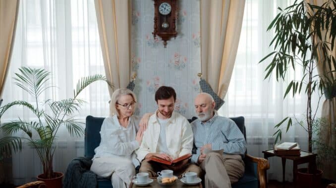 Elderly couple with son enjoying a photo album at home, sharing memories.