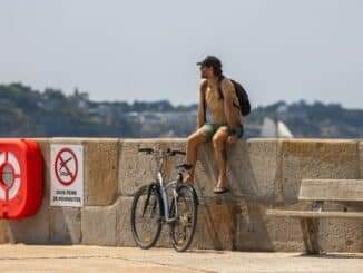 A man rests with his bicycle on the seawall in Saint-Malo, France, enjoying a sunny day.