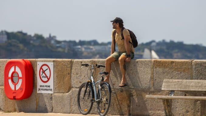 A man rests with his bicycle on the seawall in Saint-Malo, France, enjoying a sunny day.