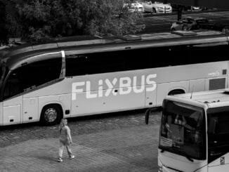 A monochrome photo of FlixBus parked at station with people nearby.