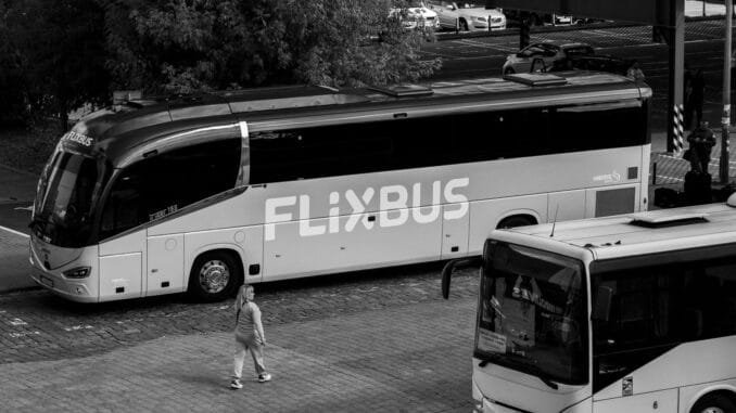 A monochrome photo of FlixBus parked at station with people nearby.
