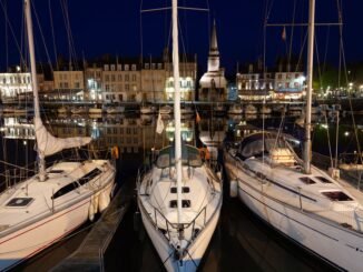 Scenic nighttime view of Honfleur marina with illuminated sailboats against a charming urban backdrop.