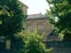 A charming stone building hidden among vibrant trees with a school sign nearby, captured on a sunny day.
