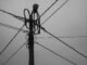 Black and white photo of a utility pole with intersecting power lines and wires.