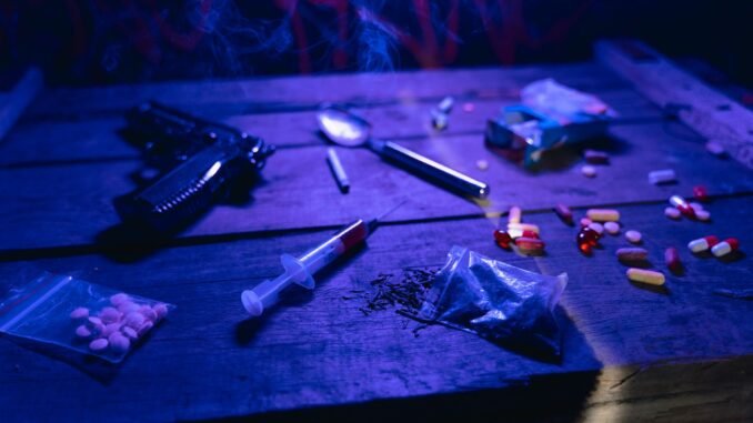 A moody scene displaying drugs, a gun, and smoke under dramatic lighting.