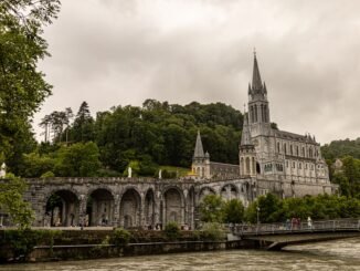 Historic cathedral in Lourdes, France amid lush greenery and stone architecture.