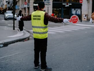 Back view of a crossing guard holding a stop sign in a busy city street.