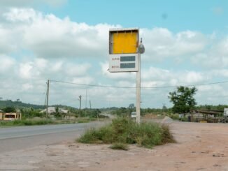 Deserted roadside gas station sign on a rural highway with cloudy sky.