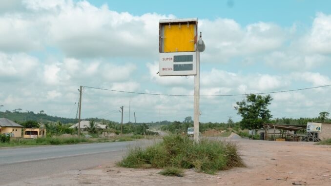Deserted roadside gas station sign on a rural highway with cloudy sky.