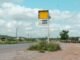 Deserted roadside gas station sign on a rural highway with cloudy sky.