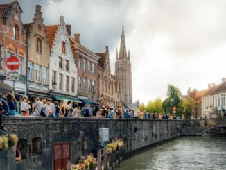 Picturesque scene of Bruges, showcasing historic buildings, a canal, and bustling crowds on a sunny day.