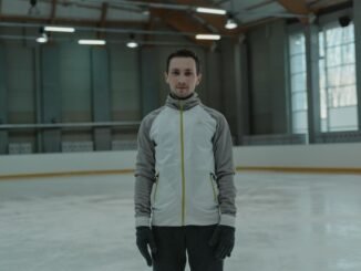A man in winter attire practicing ice skating indoors in a large arena.