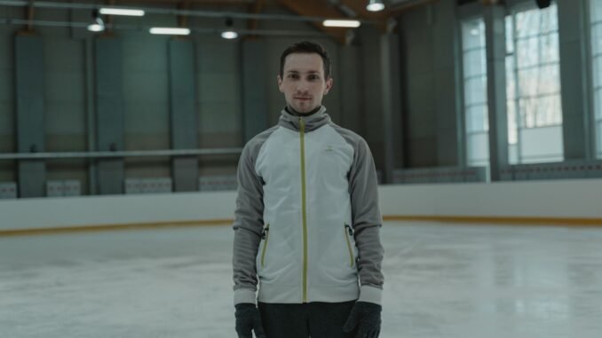 A man in winter attire practicing ice skating indoors in a large arena.
