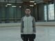 A man in winter attire practicing ice skating indoors in a large arena.