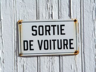 Close-up of a rustic French sign reading 'Sortie de Voiture' on a weathered white wooden wall.